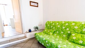 A room with a green sofa, a small plant, and a framed picture on the wall.