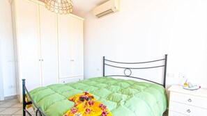 A bedroom with a green bed, a white wardrobe, and a small bedside table with a lamp.