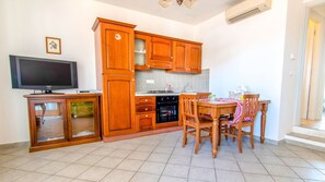 A kitchen with wooden cabinets, a dining table with chairs, a TV, and a small cabinet with a glass door.