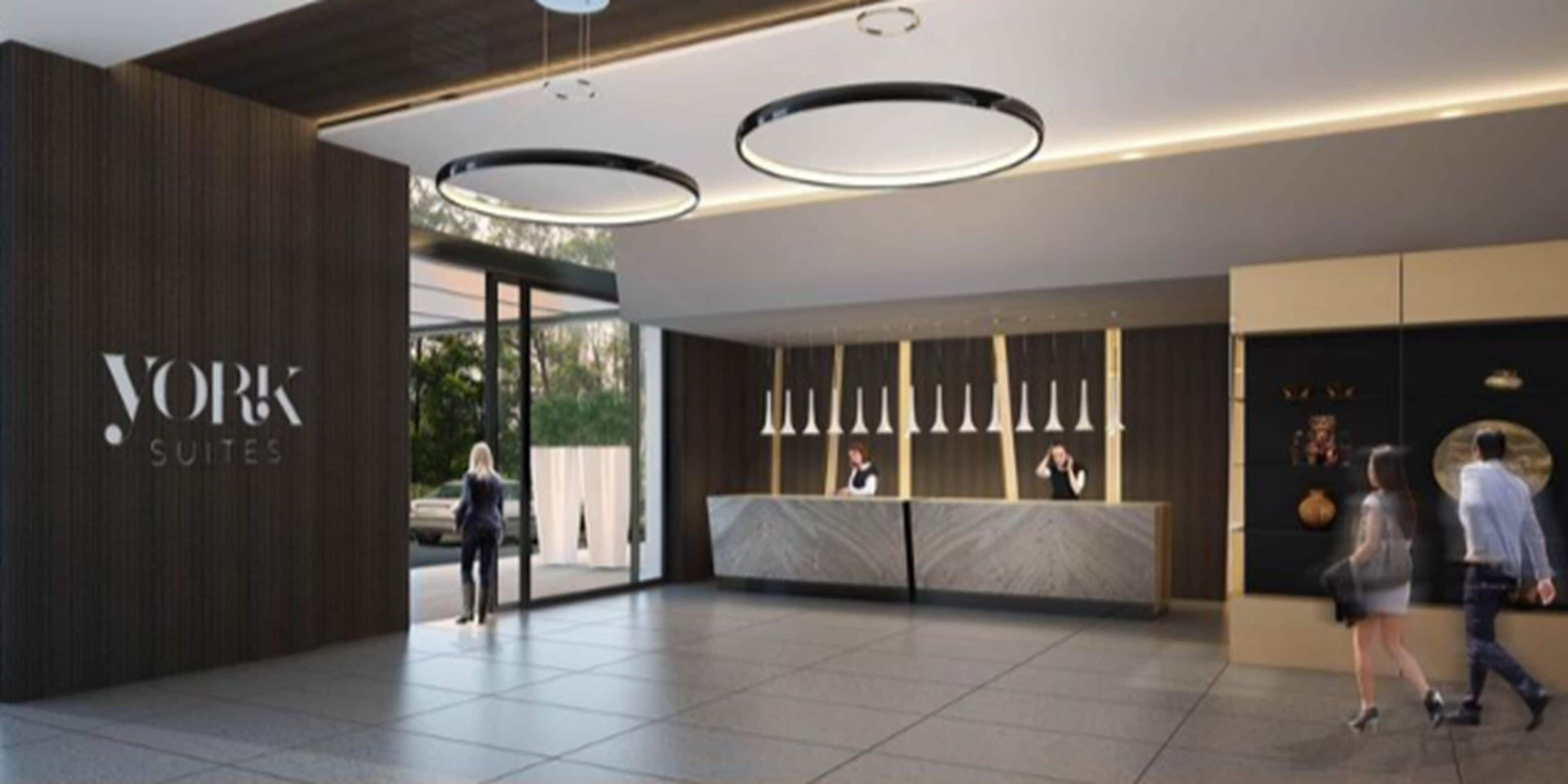A modern hotel lobby with a reception desk, a large sign for 'YORK SUITES', and a clean, contemporary design.