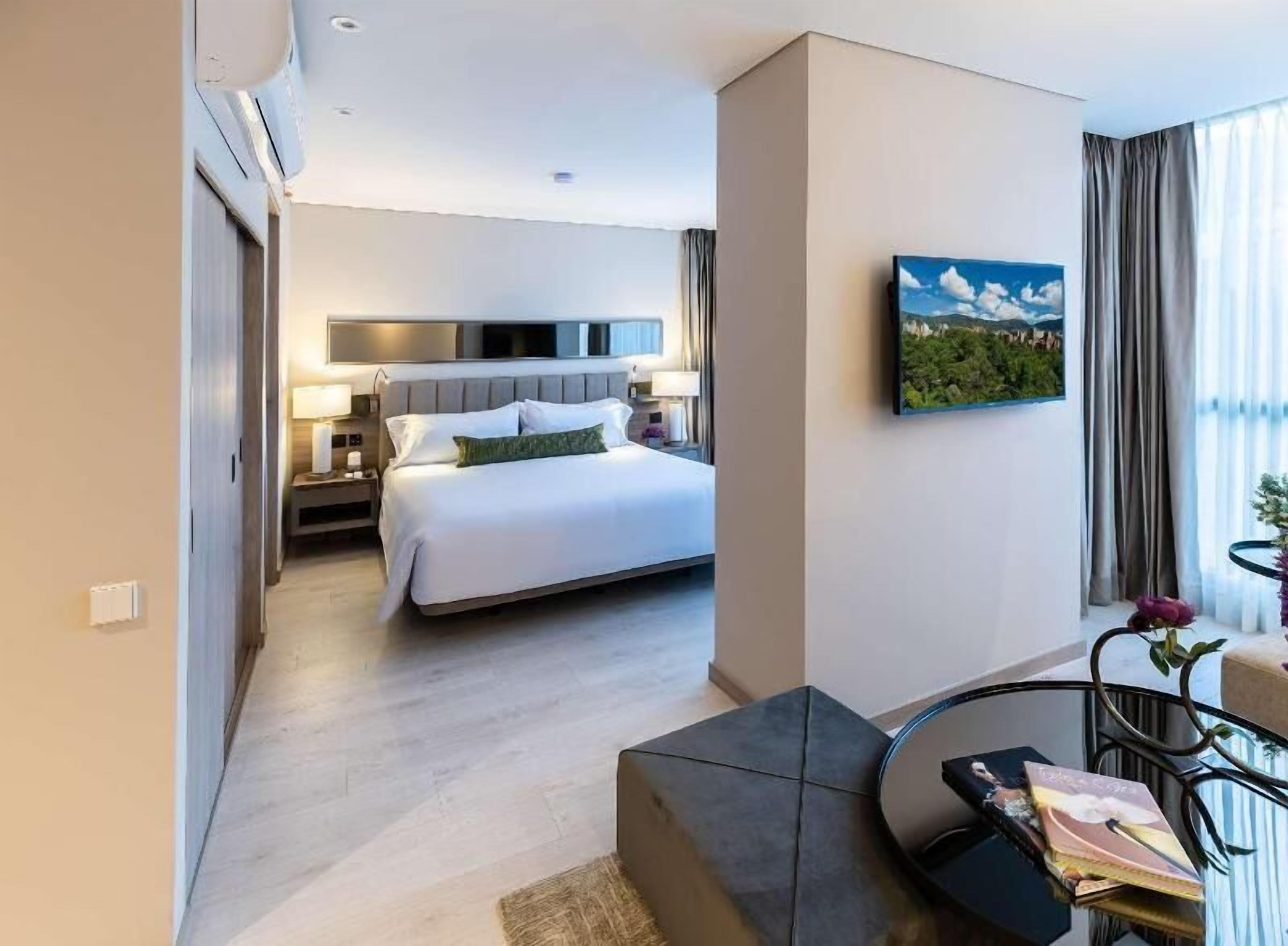 A hotel room with a bed, bedside tables, a TV, and a painting on the wall.