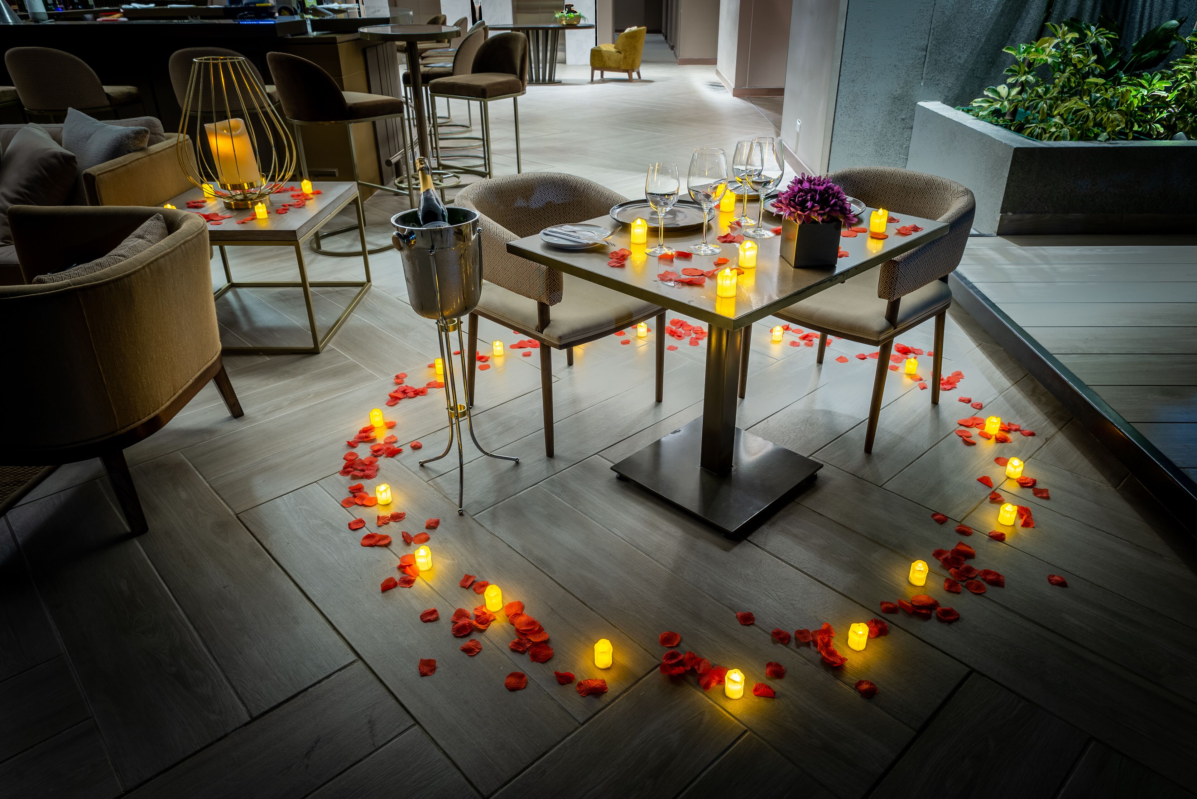 A romantic dinner setting with a table adorned with candles, rose petals, and wine glasses.