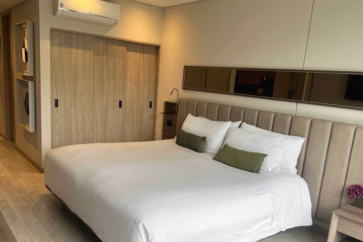 Habitación de hotel moderna con una cama grande, un armario, una mesita de noche y un televisor montado en la pared.