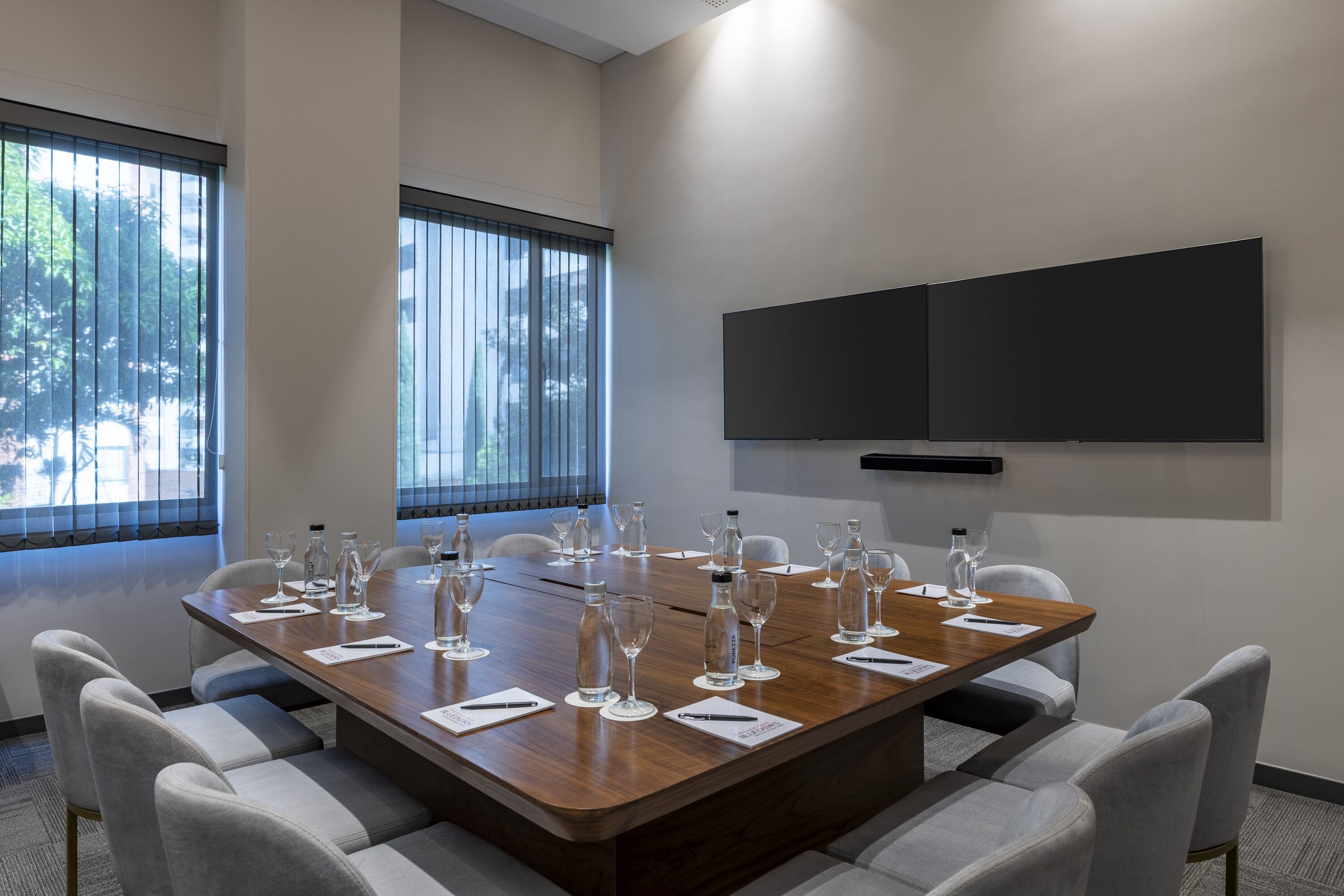 A conference room with a large table, chairs, a flat-screen TV, and windows with blinds.