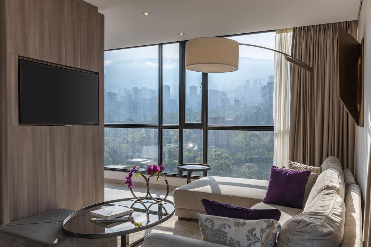 Una sala de estar moderna con un ventanal grande, un sofá, una mesa de centro y un televisor instalado en la pared.