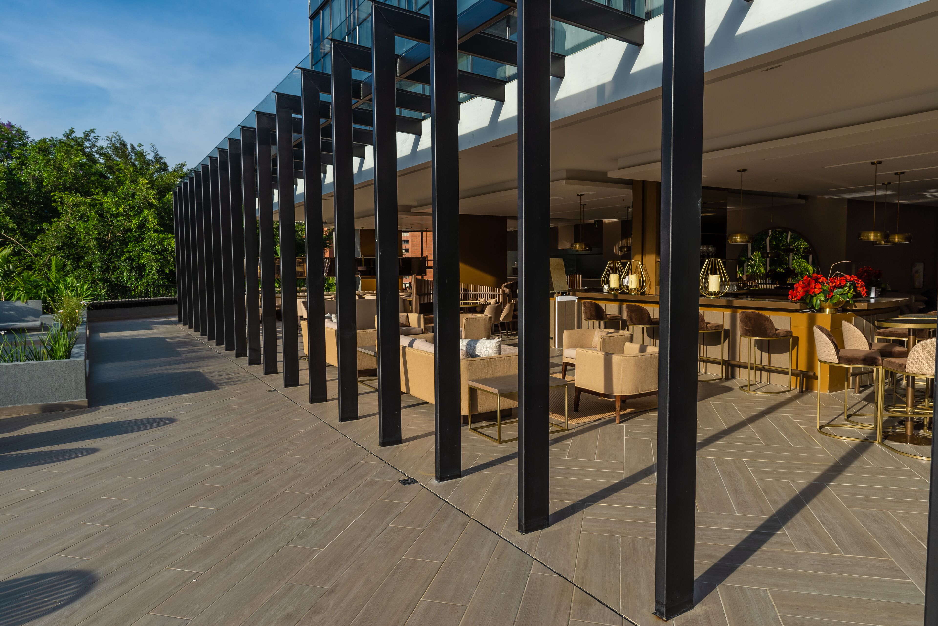 A modern outdoor seating area with multiple tables and chairs, surrounded by tall black columns, and a view of the interior through large windows.
