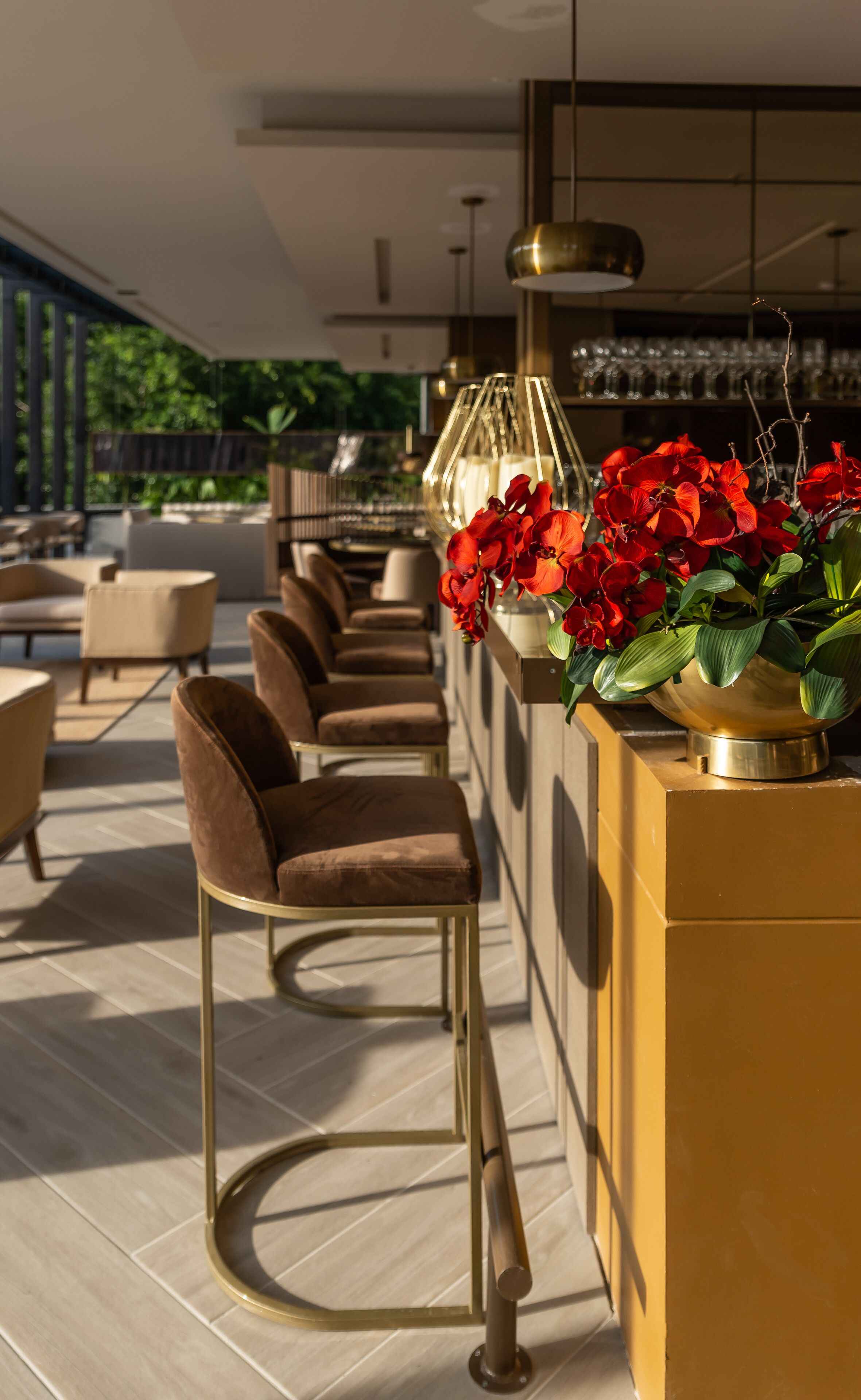A modern bar area with a row of bar stools, a gold-colored bar counter, and a vase of red flowers.