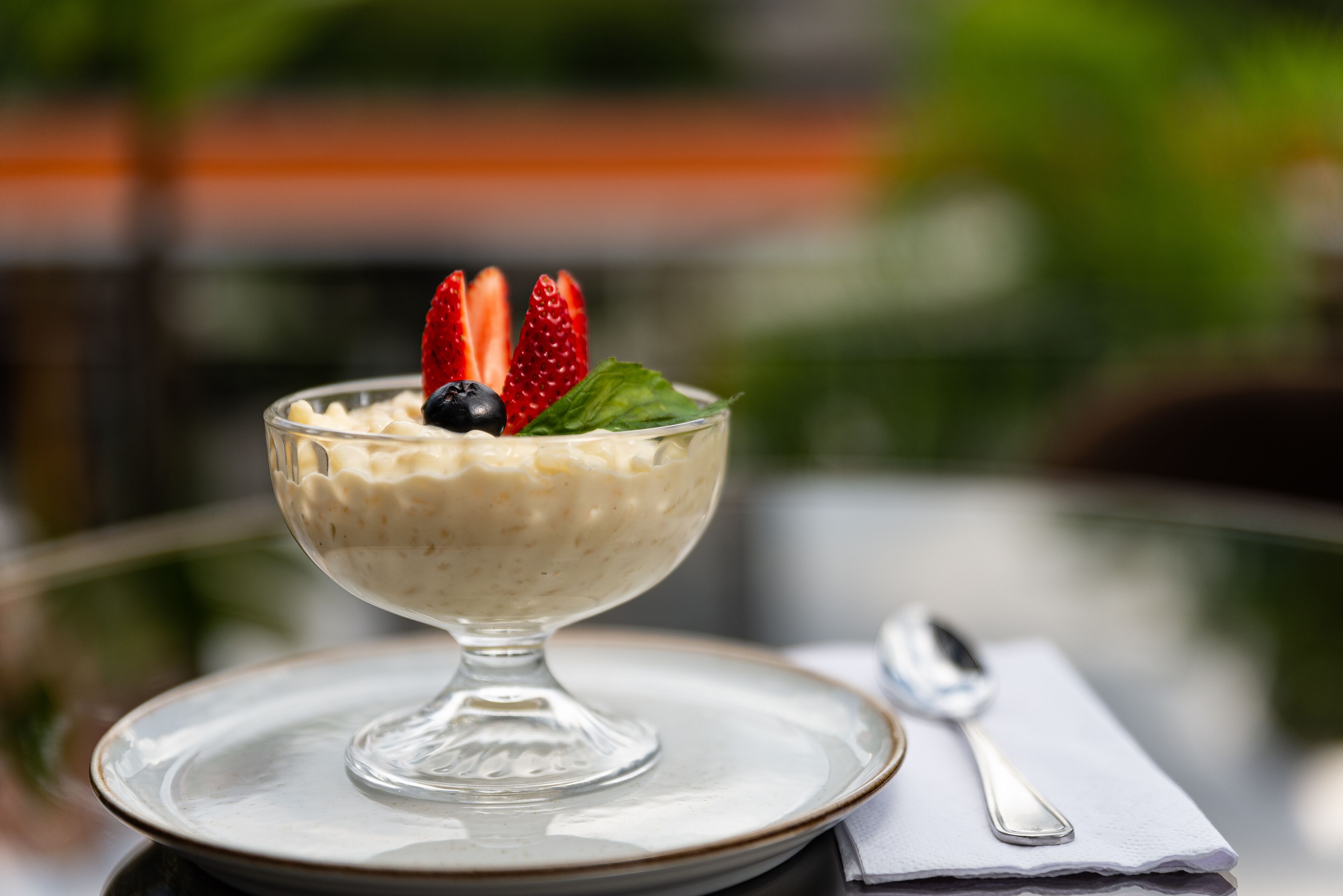 A dessert in a glass bowl on a plate with a spoon and napkin beside it.
