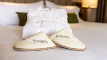 Una cama con ropa de cama blanca y una almohada verde, junto con un par de pantuflas con el texto "BLUE DOR'S".