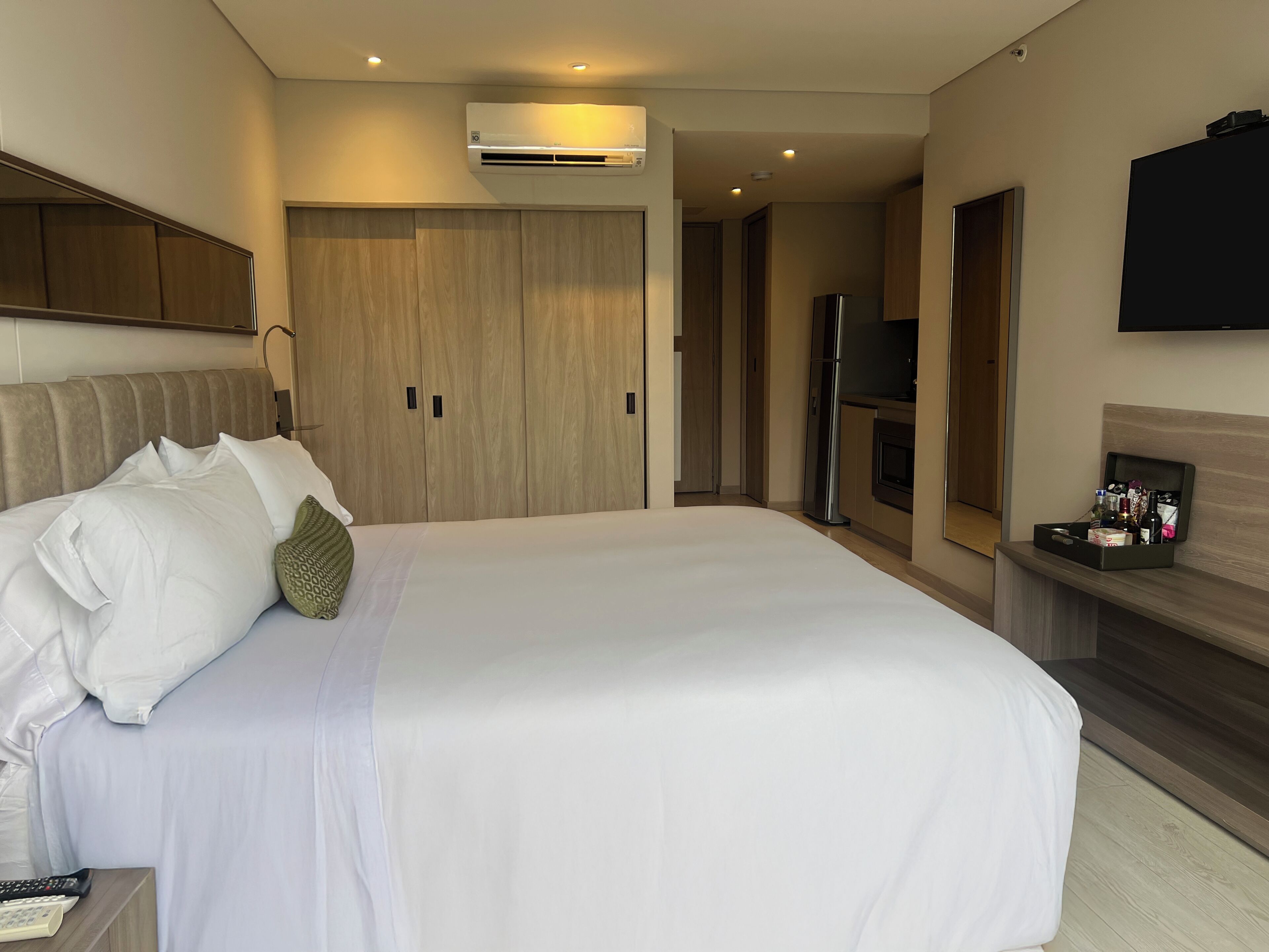 A hotel room with a large bed, a flat-screen TV, a minibar, and a built-in air conditioning unit.