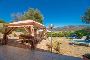 Un espace extérieur abrité, avec une table et des chaises, un lampadaire et des fauteuils de jardin bleus.