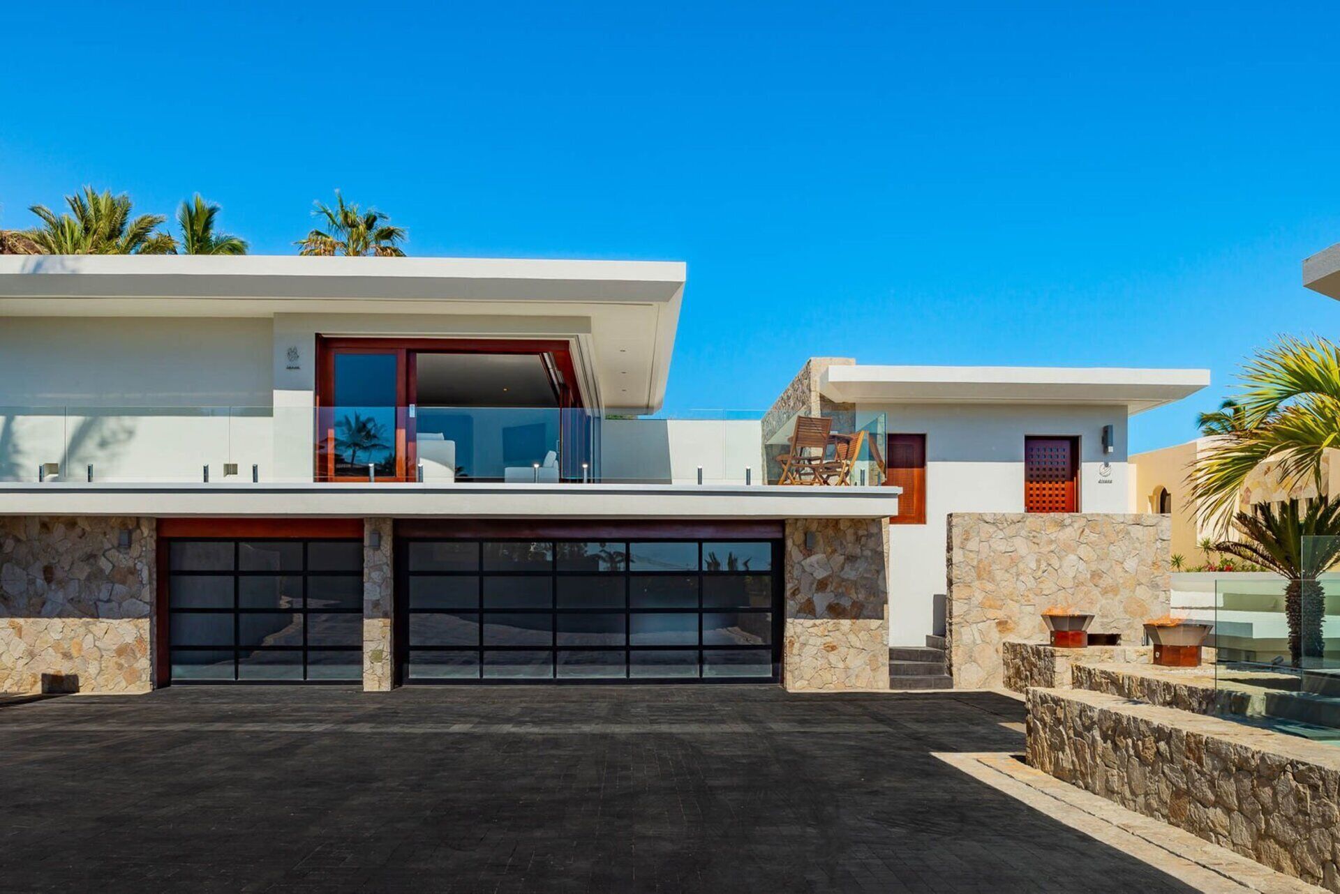 A modern two-story house with a garage, stone facade, and a clear blue sky.