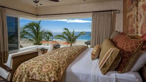 A bedroom with a large bed, a view of the beach, and a ceiling fan.