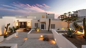 A modern building with a courtyard featuring cacti and a rock centerpiece, surrounded by white walls and minimalistic design.