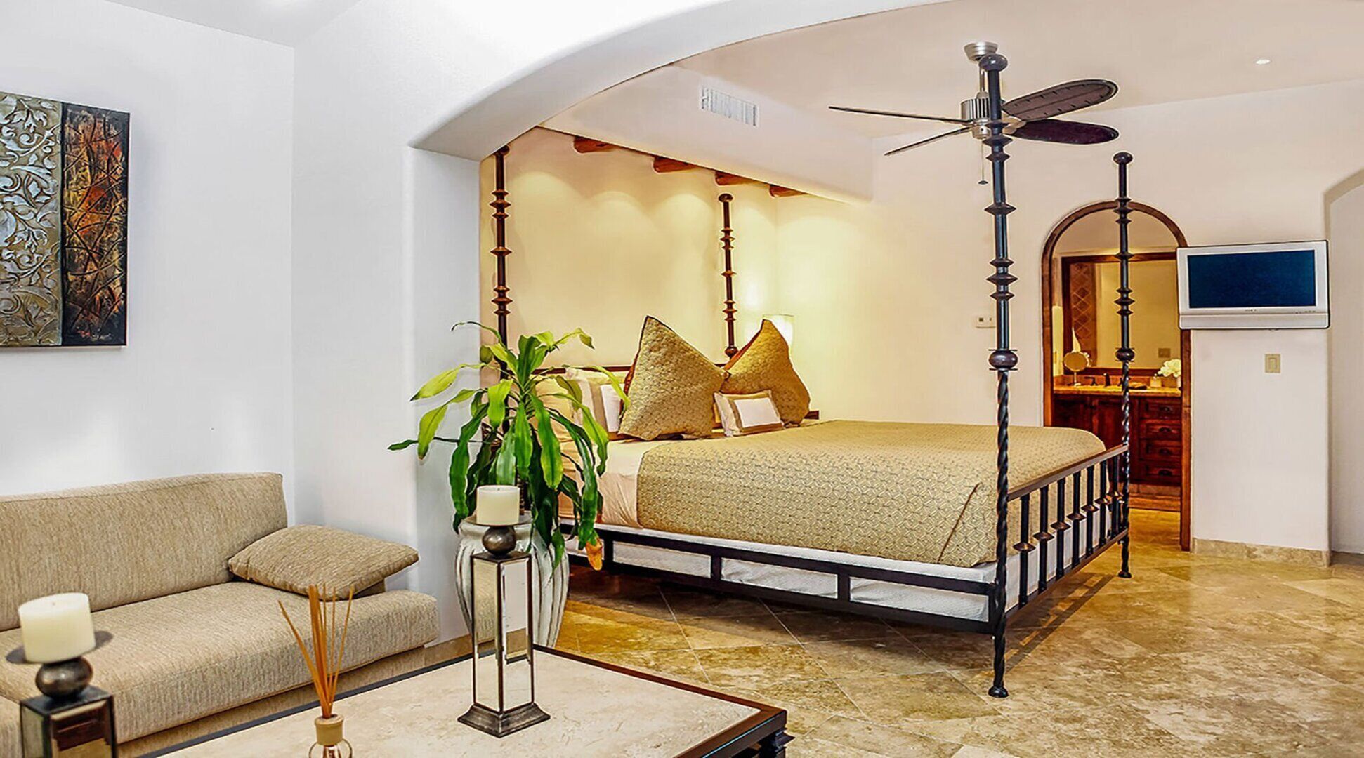 A bedroom with a four-poster bed, a sofa, a TV, and a ceiling fan.