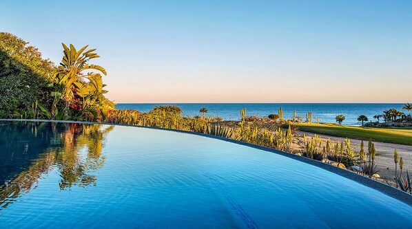 A curved infinity pool with a view of the ocean and a golf course.