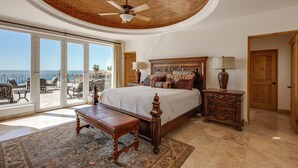 A bedroom with a large bed, a ceiling fan, a wooden nightstand, and a view of the ocean through a sliding glass door. - The Ultimate Holiday Villa in Cabo San Lucas With Private Pool and Close to the Beach, Cabo San Lucas Villa 1011 (Cabo San Lucas)