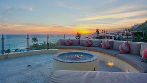 A curved sofa with colorful cushions, a circular fire pit, and a view of the ocean at sunset. - The Ultimate Holiday Villa in Cabo San Lucas With Private Pool and Close to the Beach, Cabo San Lucas Villa 1011 (Cabo San Lucas)