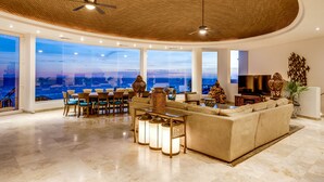 A spacious living area with a high ceiling, large windows offering a view of the ocean, a comfortable sofa, and a dining area with chairs and tables. - The Ultimate Holiday Villa in Cabo San Lucas With Private Pool and Close to the Beach, Cabo San Lucas Villa 1011 (Cabo San Lucas)