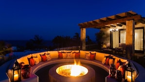 A circular outdoor seating area with a fire pit, surrounded by cushions and lanterns, under a wooden pergola with a view of the ocean. - Beautiful Holiday Villa in a Prime Location in Cabo San Lucas 1007 (Cabo San Lucas)