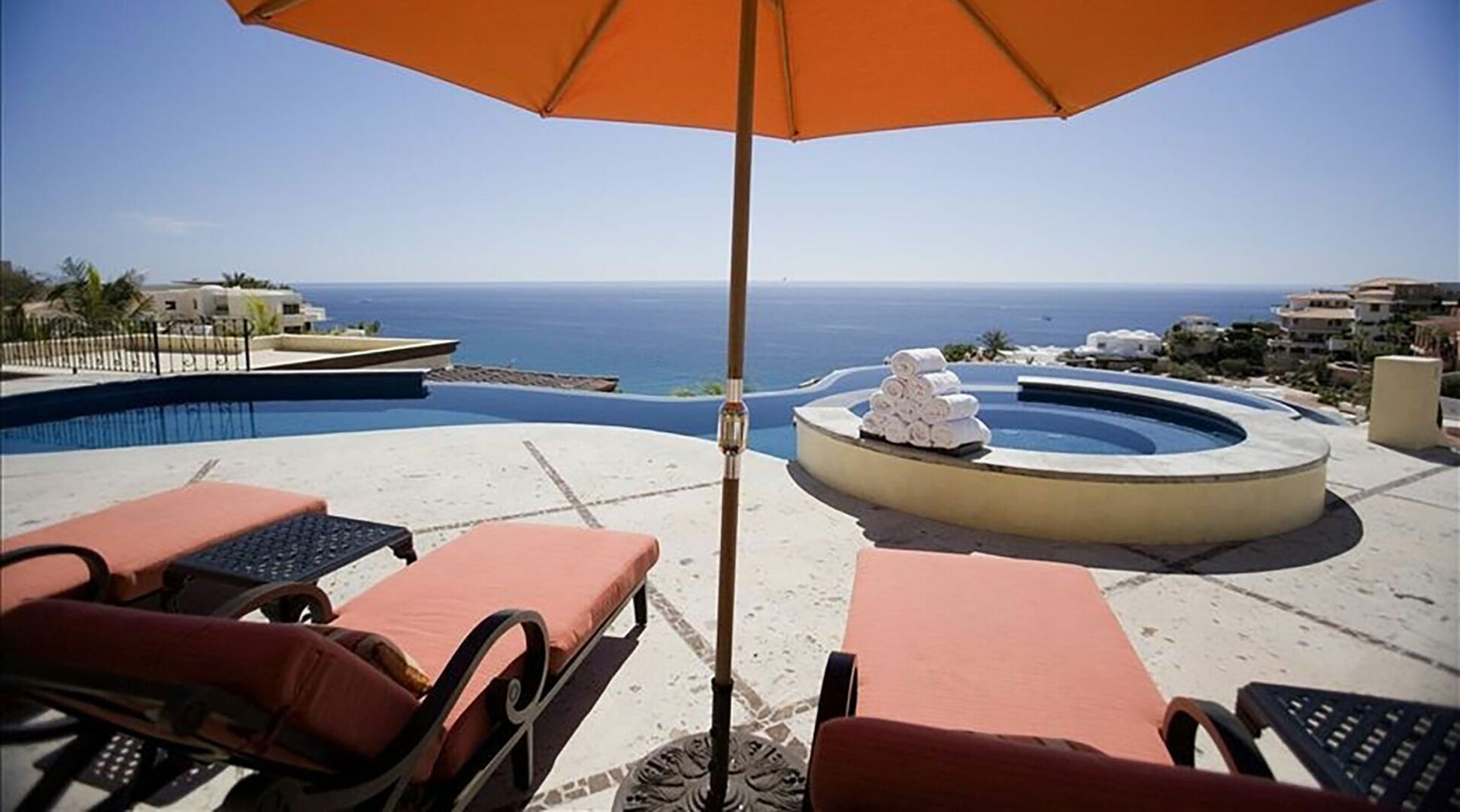Ein Poolbereich mit Liegestühlen und Sonnenschirm, mit Blick auf das klare, blaue Meer.