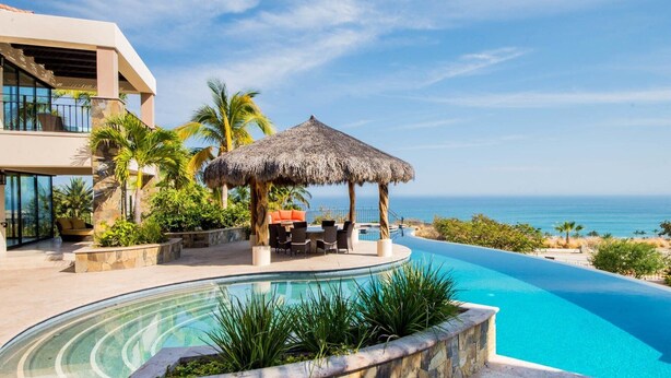 Um resort com piscina, uma construção de colmo e vista para o oceano.