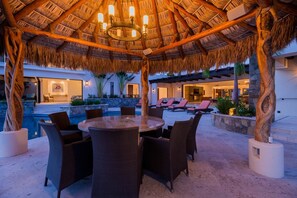 Un patio exterior con techo de paja, piscina y sillones de descanso.
