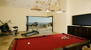 Una habitación con mesa de billar, equipo de ejercicio y televisor.