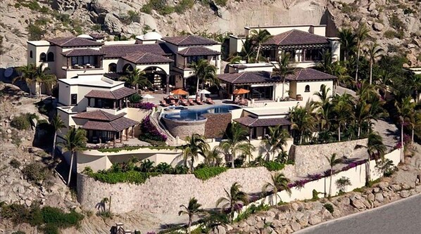 Un complejo turístico con varias edificaciones, una piscina central y palmeras.