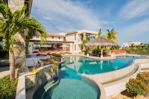 Un resort con una amplia piscina, mobiliario exterior y una estructura de techo de paja.