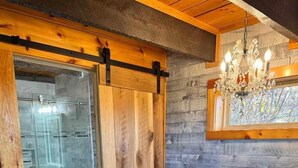 A rustic bathroom with a freestanding bathtub, wooden door, and a glass shower enclosure. - The Man o' War at Jayell Ranch (Sevier County)