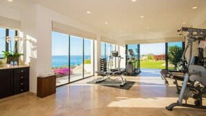 A spacious room with large windows offering a view of the ocean, a treadmill, and a weight bench.