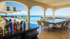A bar area with a view of the ocean, outdoor seating, and a pool.
