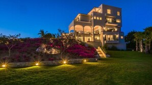 A multi-story modern building with a well-lit entrance and a landscaped garden with pink flowers.