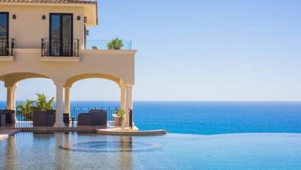 A hotel with a pool overlooking the ocean, featuring a balcony with outdoor seating.
