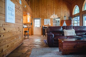 Ein gemütliches Holzhaus-Interieur mit einer Ledersofa, Steinböden und einem Essbereich, der durch eine offene Tür erkennbar ist.