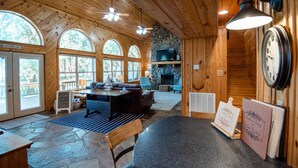 A cozy cabin interior with wooden walls, a stone fireplace, a dining area, and large windows. - *Waterfront* charming cabin w/ private boat dock (Bullard)