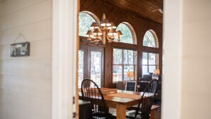 A wooden dining area with a table and chairs, large arched windows, and a chandelier. - *Waterfront* charming cabin w/ private boat dock (Bullard)