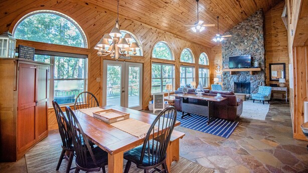 A wooden cabin interior with a dining area, stone fireplace, and large windows. - *Waterfront* charming cabin w/ private boat dock (Bullard)