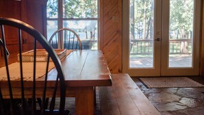 A wooden dining table with chairs, a stone floor, and a view of an outdoor deck through a glass door. - *Waterfront* charming cabin w/ private boat dock (Bullard)