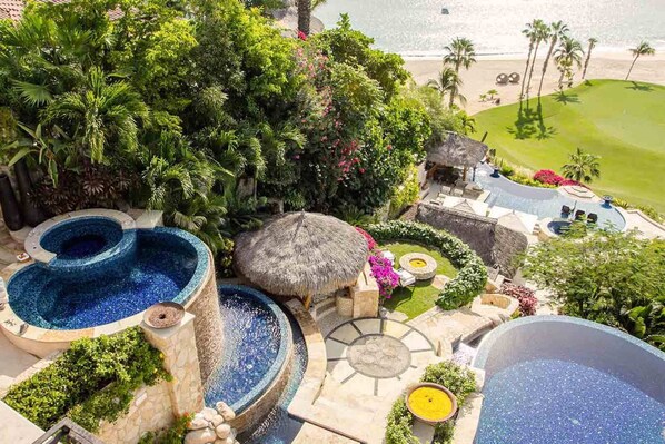 A luxurious resort with multiple swimming pools, a thatched-roof structure, and a view of the beach.
