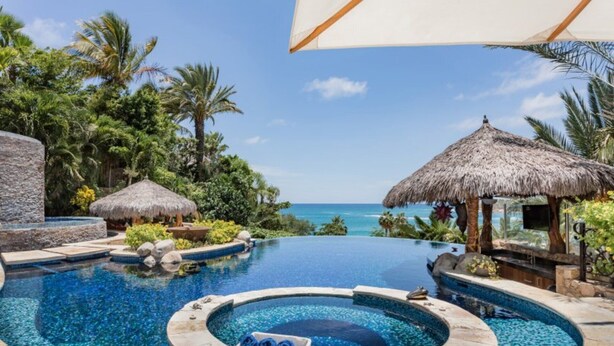 A pool area with a view of the ocean, surrounded by tropical vegetation and thatched-roof structures. - The Ultimate Holiday Villa in San José del Cabo With Private Pool and Close to the Beach, San Jose Del Cabo Villa 1008 (San José del Cabo)