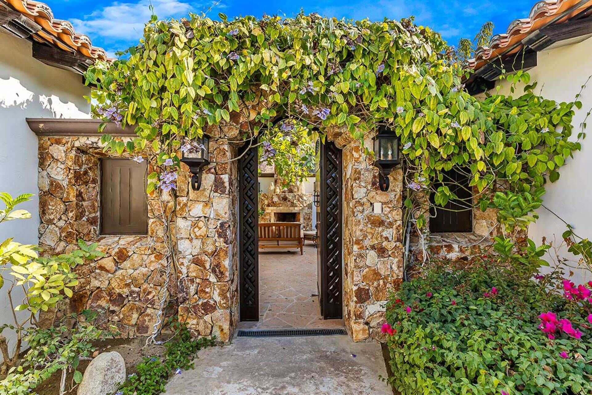 A stone building with a covered entrance, a wooden bench inside, and surrounding greenery.