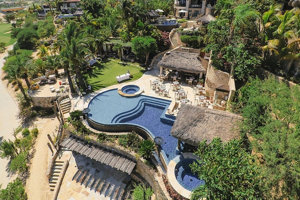 A resort with a large swimming pool, outdoor seating areas, and lush greenery.