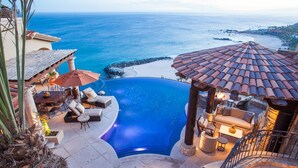 Ein luxuriöser Infinity-Pool mit Meerblick, Sitzgelegenheiten im Freien und einem Steinkamin.