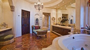 Een luxe badkamer met een ruime badkuip, een houten bankje, een kroonluchter en een decoratieve spiegel.
