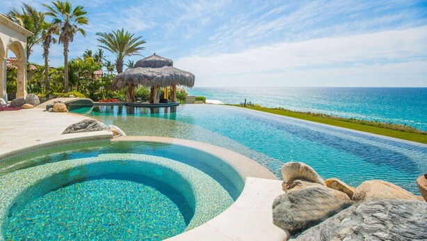 A infinity pool with a clear view of the ocean, surrounded by rocks and palm trees. - Luxury Holiday Villa near Main Attractions, San Jose del Cabo Villa 1019 (San José del Cabo)