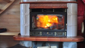 A fireplace with a stone base, a wooden mantel, and a red wall behind it. - Chalet Alpinka (Cerklje na Gorenjskem)
