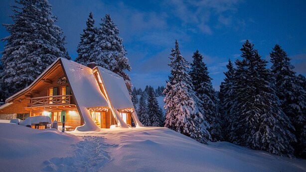 A log cabin with a snow-covered roof and a balcony, surrounded by snow-laden trees. - Chalet Alpinka (Cerklje na Gorenjskem)