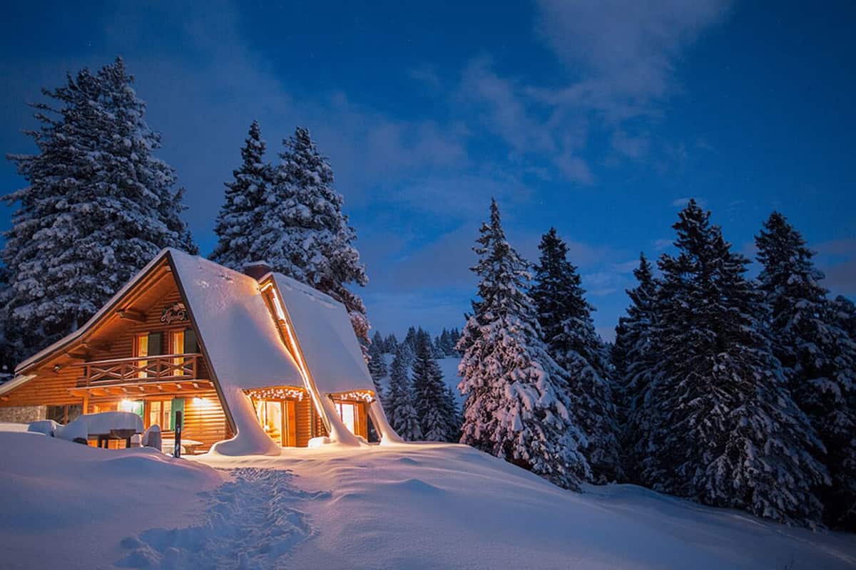 Eine Blockhütte mit schneebedecktem Dach und einem Balkon, umgeben von schneelastigen Bäumen.